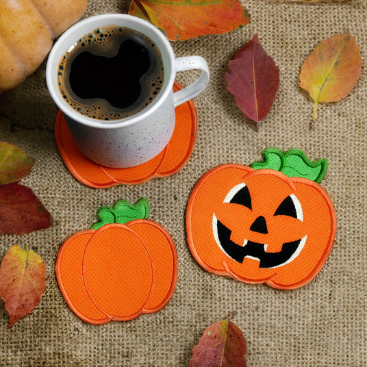 Pumpkin-shaped coasters with a cup of coffee on a burlap surface with leaves.