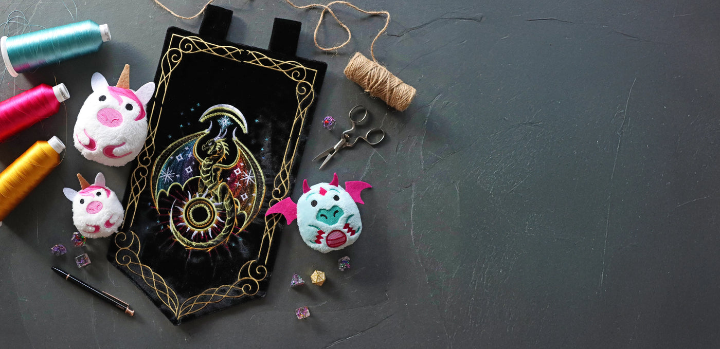 Black flag with machine embroidered celestial dragon and gold borders, staged with machine embroidered in-the-hoop dragon stuffies and various crafting supplies.