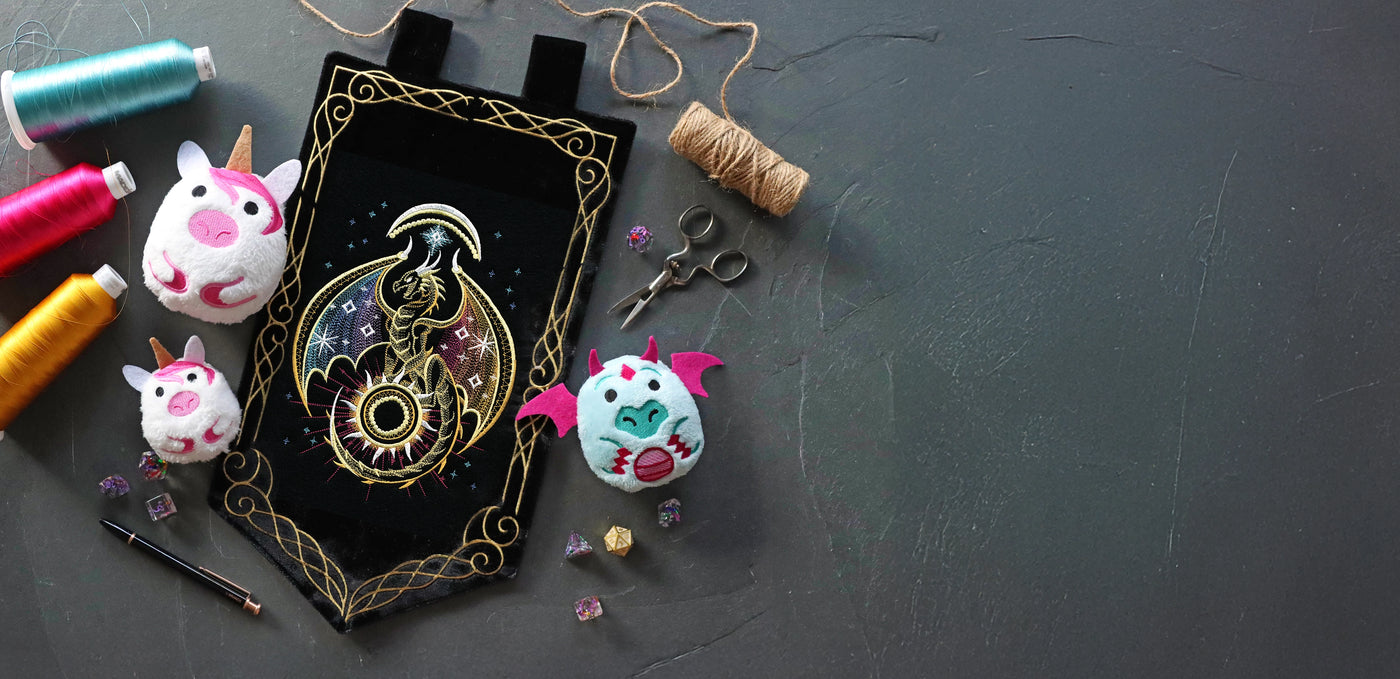 Machine embroidered celestial dragon on a black wall hanging surrounded by in-the-hoop unicorn and dragon plushies.
