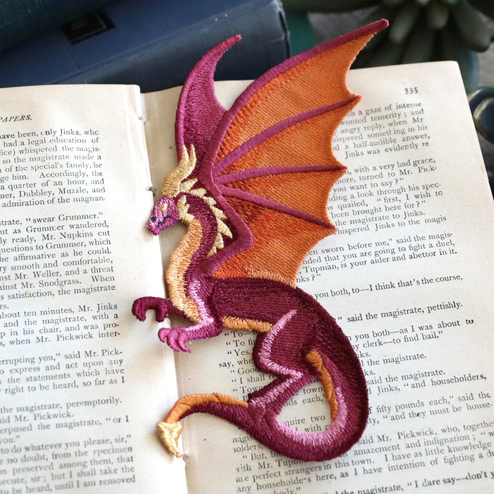 Machine embroidered freestanding dragon laying on a book