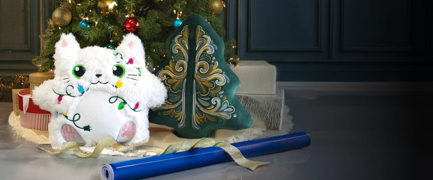 machine embroidery plush Christmas cat and flourish design on pillow next to a tree