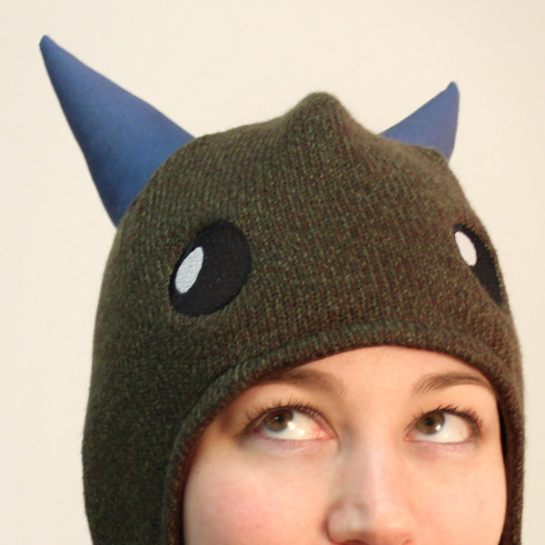 Green hat with blue embroidered horns and cartoon eyes, shown as a finished Monster Factory embroidery Design Pack project.