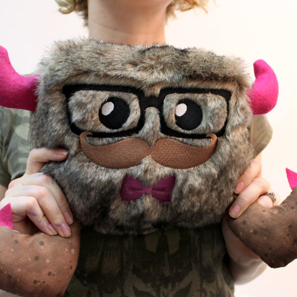 A plush featuring a digitally downloadable machine embroidery Design Pack with bold embroidered features is held up.