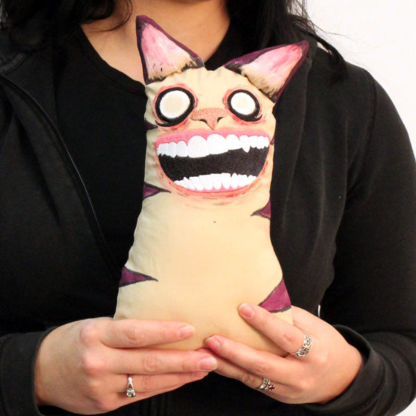 Close-up of a plush toy embroidered with wide eyes, a big grin, and pointed ears; part of the Design Pack is visible.
