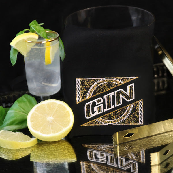 Black tea towel with 'GIN' machine embroidery design next to a gin cocktail with lemon and mint.