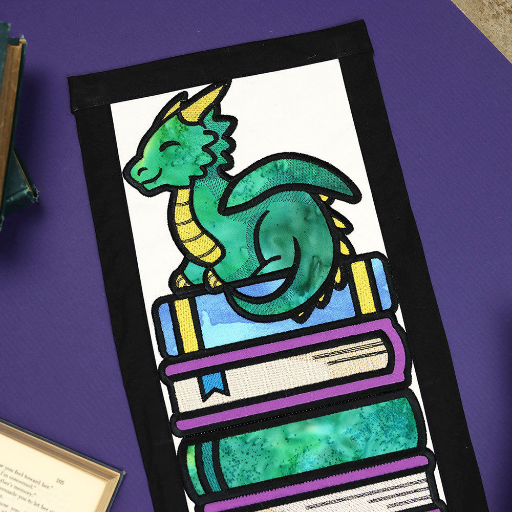 Embroidered green dragon sitting on a stack of books, part of a digitally downloadable machine embroidery Design Pack.