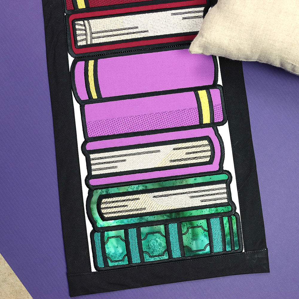 Embroidered applique of a fabric stack of books with a small pillow, in the Book Stack Buddies digitally downloadable design.