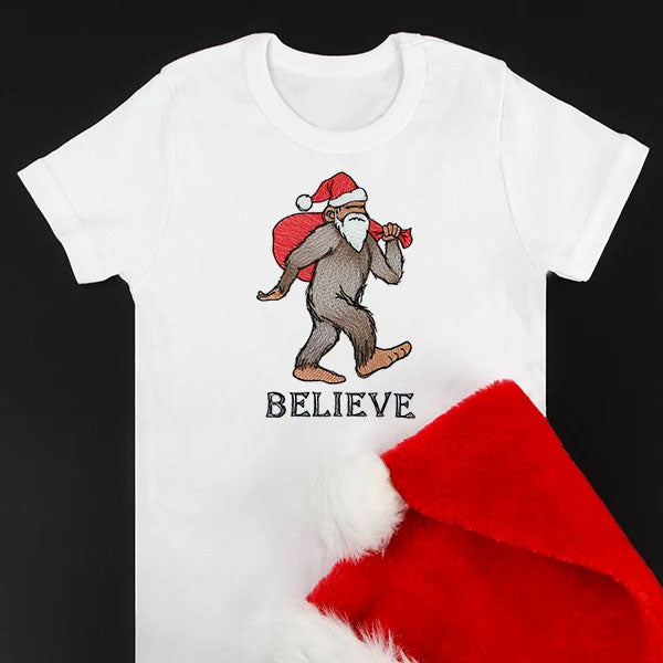 Digitally downloadable machine embroidery design of a Bigfoot wearing a Santa hat and beard, carrying a red sack, with the word "BELIEVE" below.