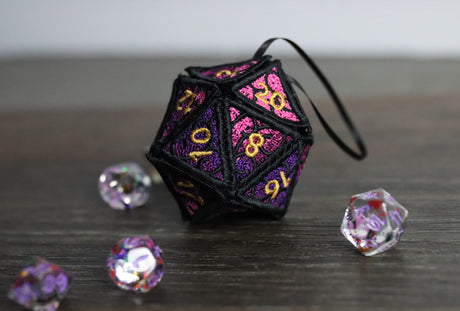 Machine embroidered 3D Lace D20 ornament surrounded by dice on a wooden table