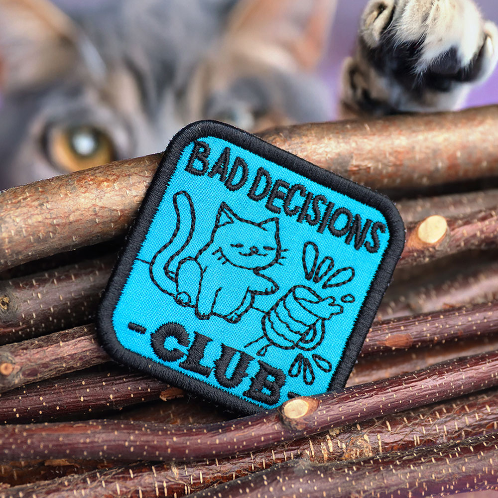 Machine embroidery in-the-hoop patch with text 'Bad Decisions Club' by wood sticks.