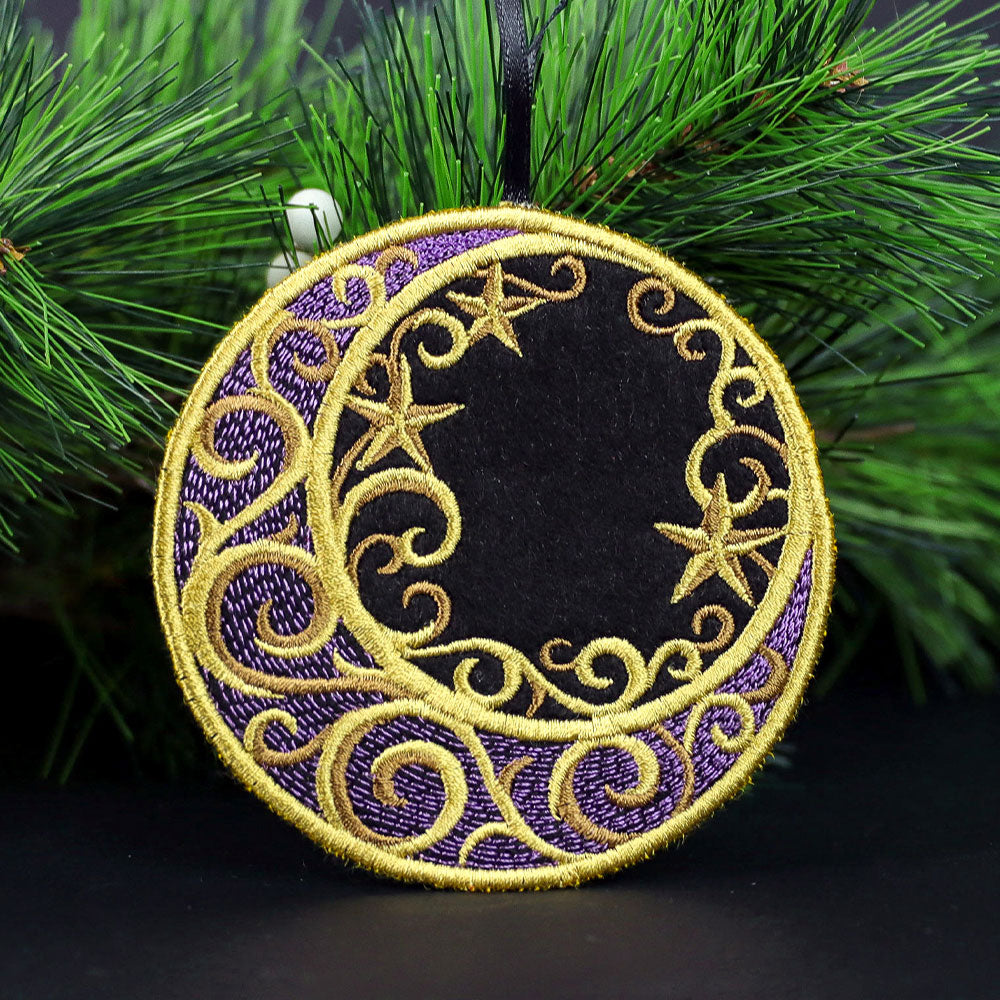 Round embroidered ornament in purple and black with gold crescent moon, stars, and swirl designs hanging on green pine branch.