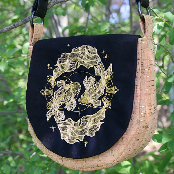 Embroidery design featuring metallic koi fish and stars on cork and black fabric, shown on a finished bag.
