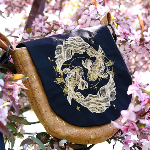 Metallic koi fish are embroidered on contrasting black and tan fabric, shown on a finished Celestial Koi Pond bag.