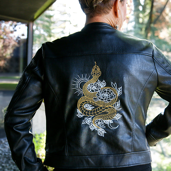 Black leather jacket with machine embroidered gold and white snake design on the back, outdoors.