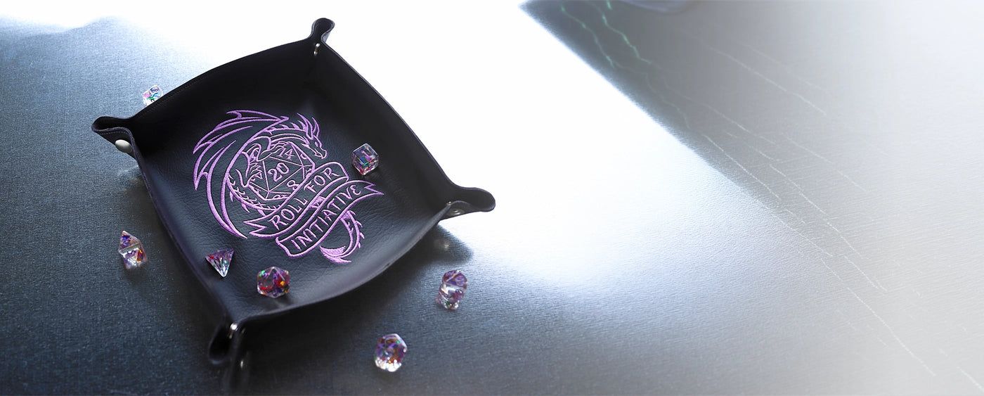 Black decorative dice tray with machine embroidered purple dragon design on a staged on a reflective surface