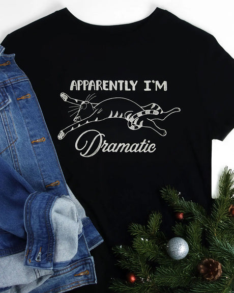 Black t-shirt with white graphic and text 'Apparently I'm Dramatic' next to a denim jacket and Christmas tree.
