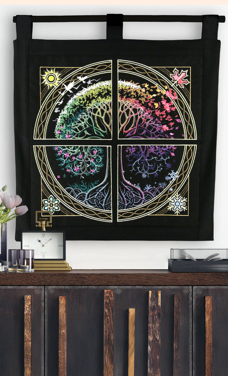 Colorful machine embroidery tree panel design on black fabric hanging on a white wall by a home decor items.