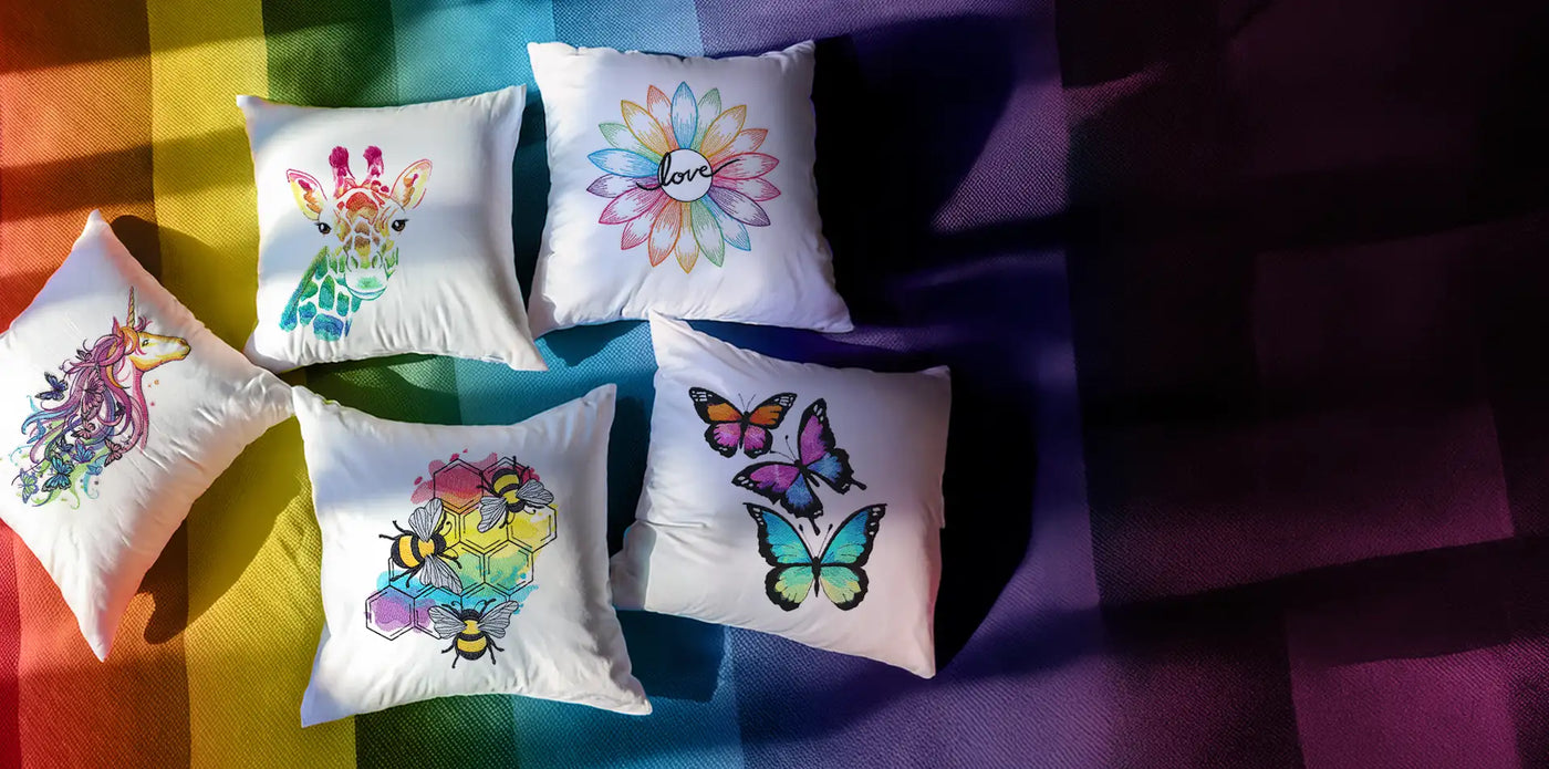Machine embroidery rainbow designs on white pillows against a rainbow background