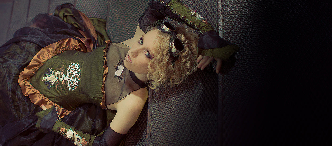 Steampunk styled model with a machine emrboidered dress with intricate clothing and accessories on a dark background