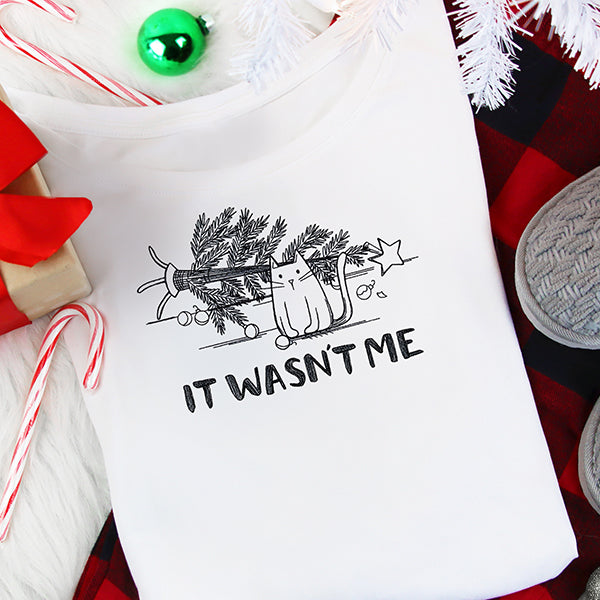 Embroidery design shows a kitten beside a fallen tree with the text IT WASNT ME stitched below.