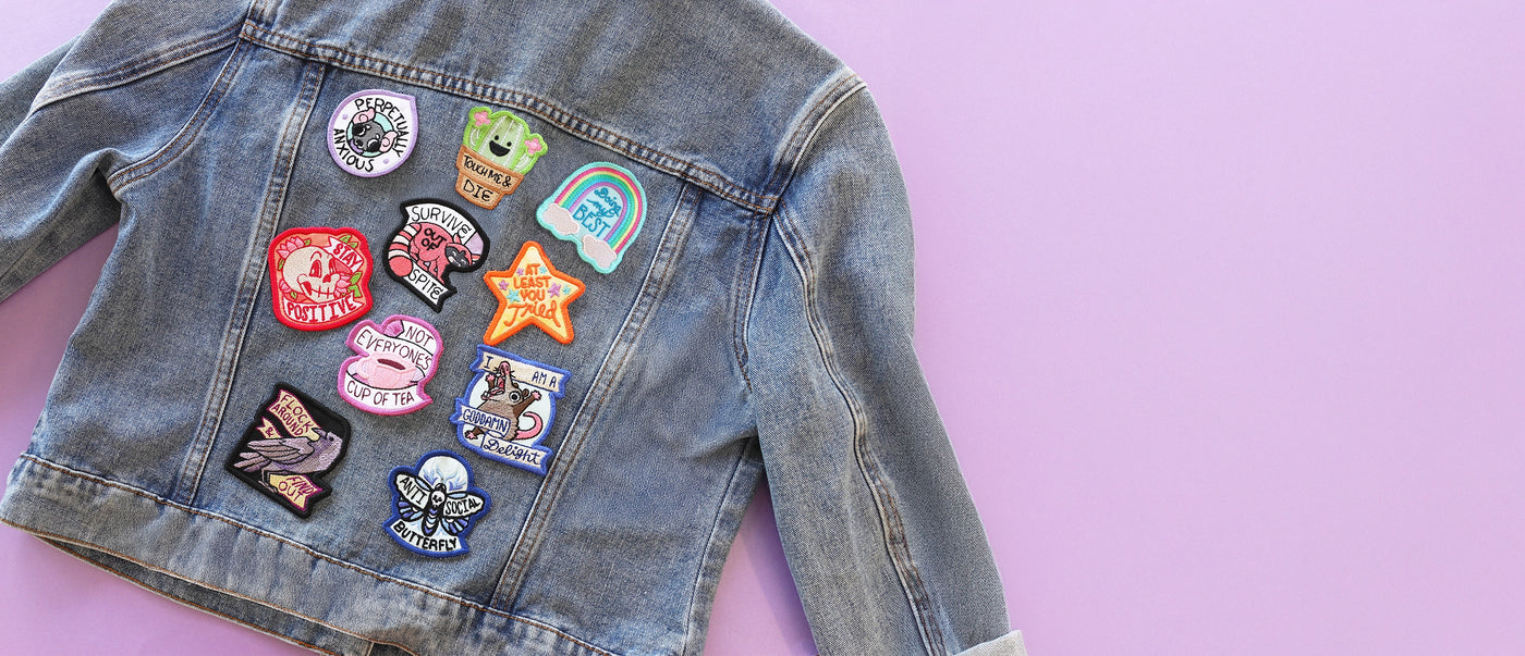 Denim jacket with various machine embroidery patches on a pink background