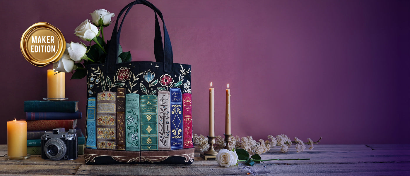 Machine embroidery book design on black tote surrounded by books on a wooden table.