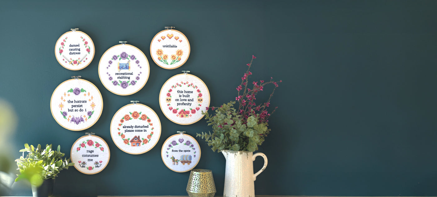 Decorative sassy machine embroidery designs inspired by cross-stitch in embroidery hand hoops on green wall.