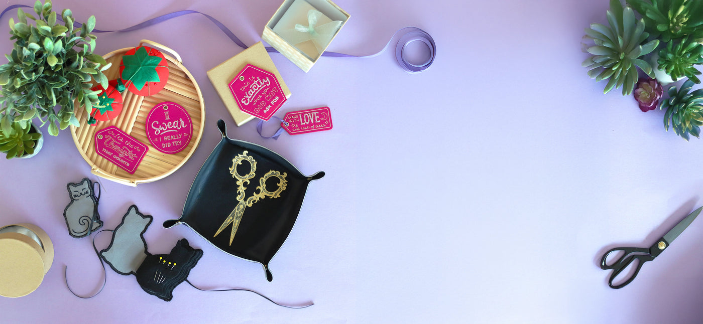Machine embroidery tags, cat needlebook and scissor design in tray on a purple background