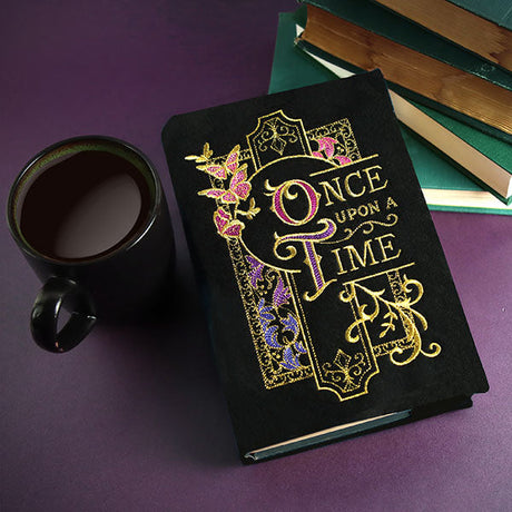 Gold and pink embroidery forms a filigree design on a black book cover, shown as a finished project.