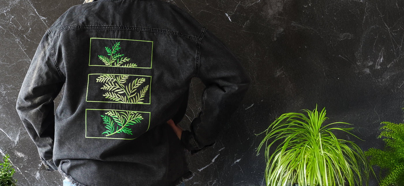 Person wearing a black jacket with a machine embroidery green leaf design on a dark background