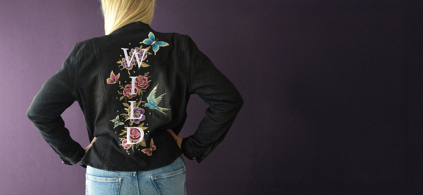 Person wearing a black jacket with machine embroidery floral and butterfly designs on the back against a purple background