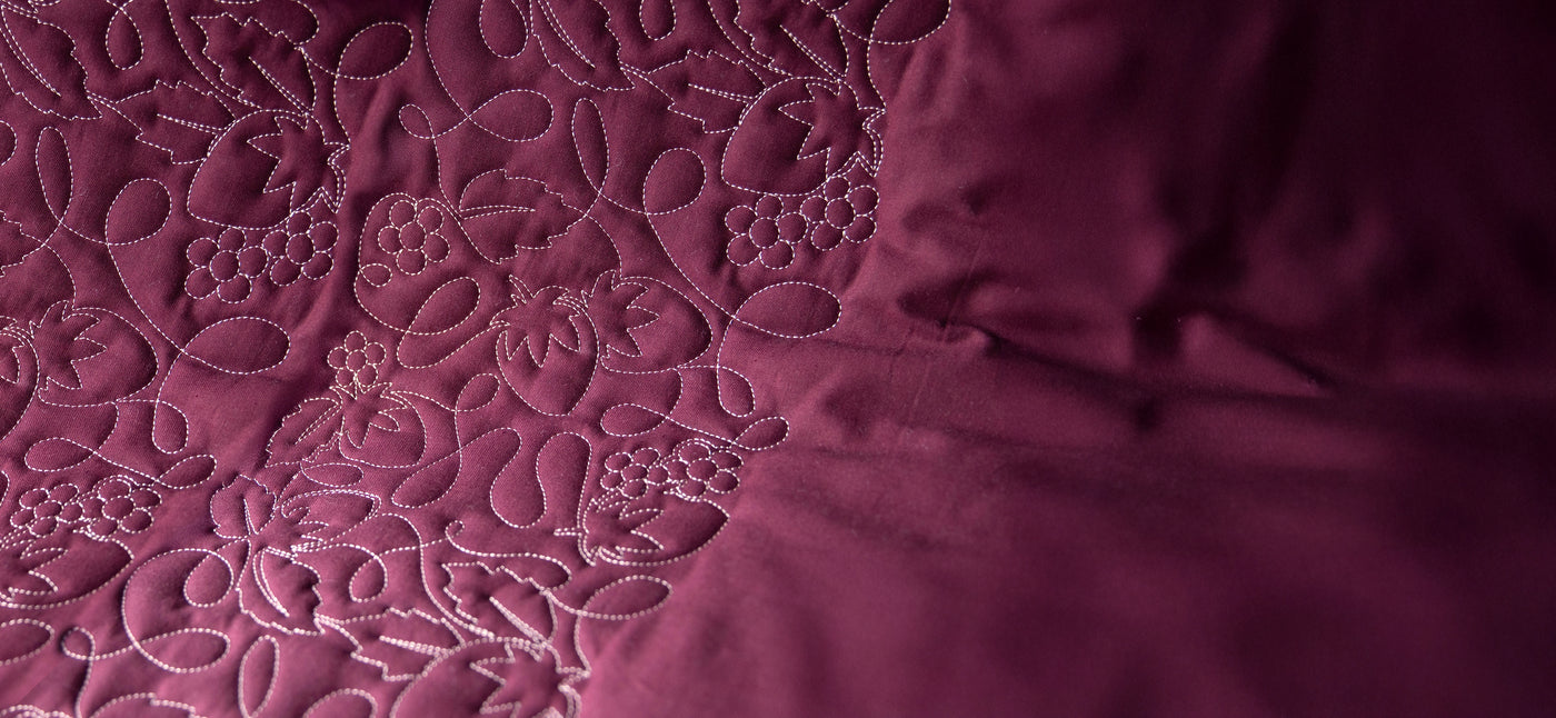 Close up of machine embroidery edge-to-edge berries and flowers on purple fabric