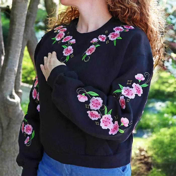 Person wearing a black sweatshirt with pink floral embroidery in an outdoor setting