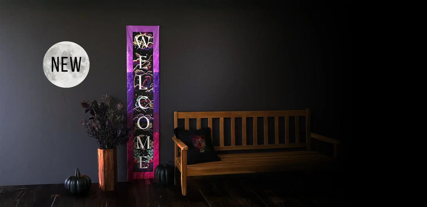 Purple and black Halloween-themed “Welcome” banner, displayed on a dark wall next to a wooden bench and autumn decor.