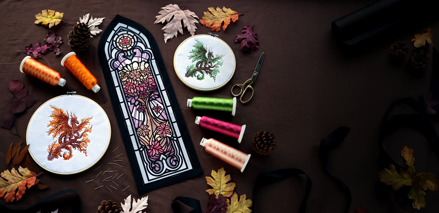 Stained glass nature design and embroidery hoops with dragon designs and spools of thread on a dark surface.