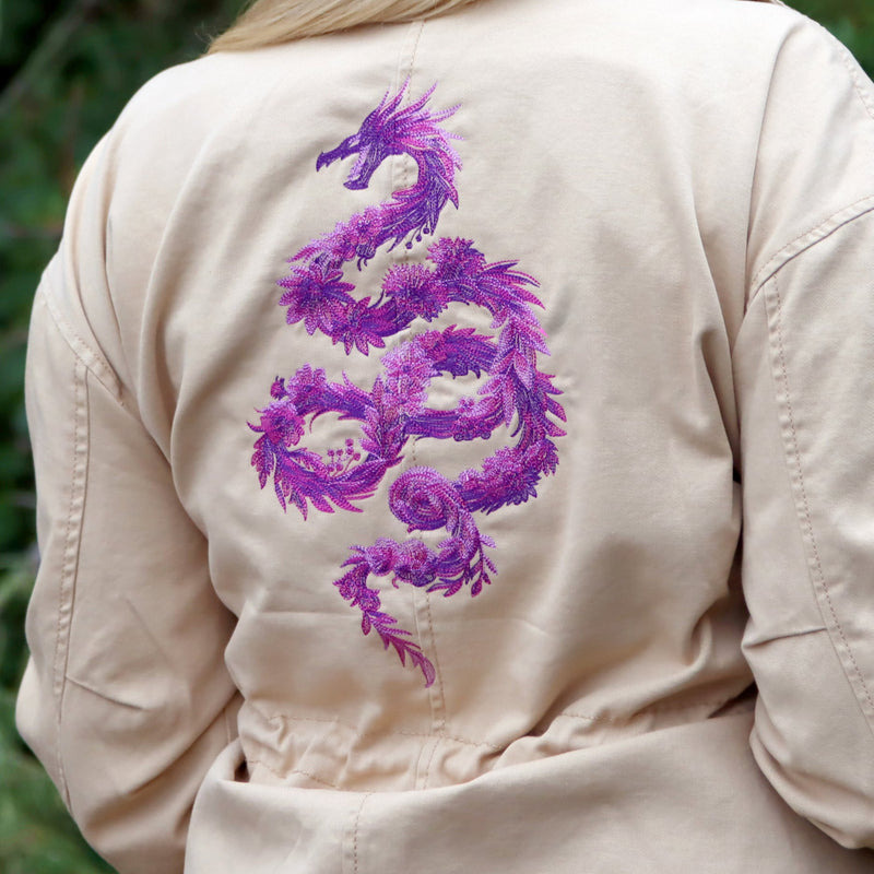 Beige jacket with a purple dragon design on the back against a blurred green background