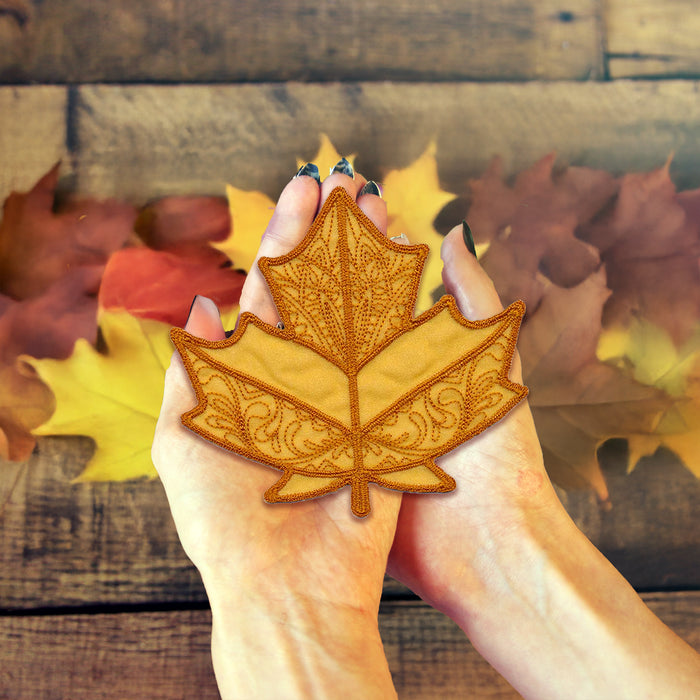 Hand holding a decorative leaf against a wooden background with autumn leaves.