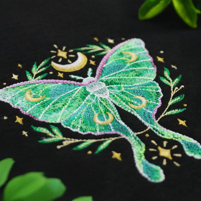 Embroidered celestial butterfly design on a black background with stars and moons.
