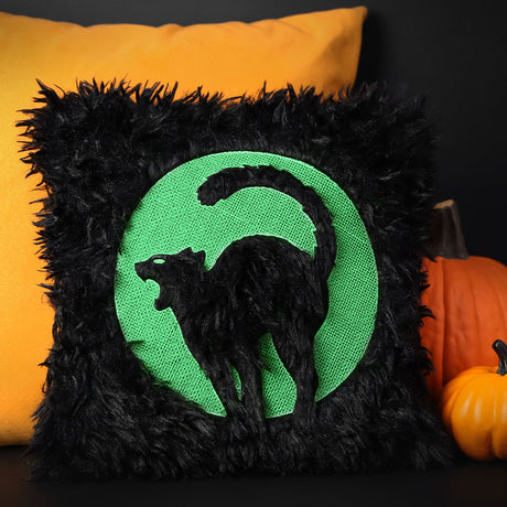 Black pillow with a machine embroidered embossed cat design a cat and moon, against an orange pillow and pumpkin background.