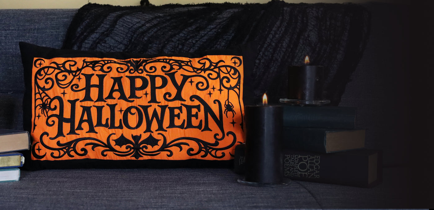 Decorative pillow with 'Happy Halloween' text on an orange background, placed on a dark surface.