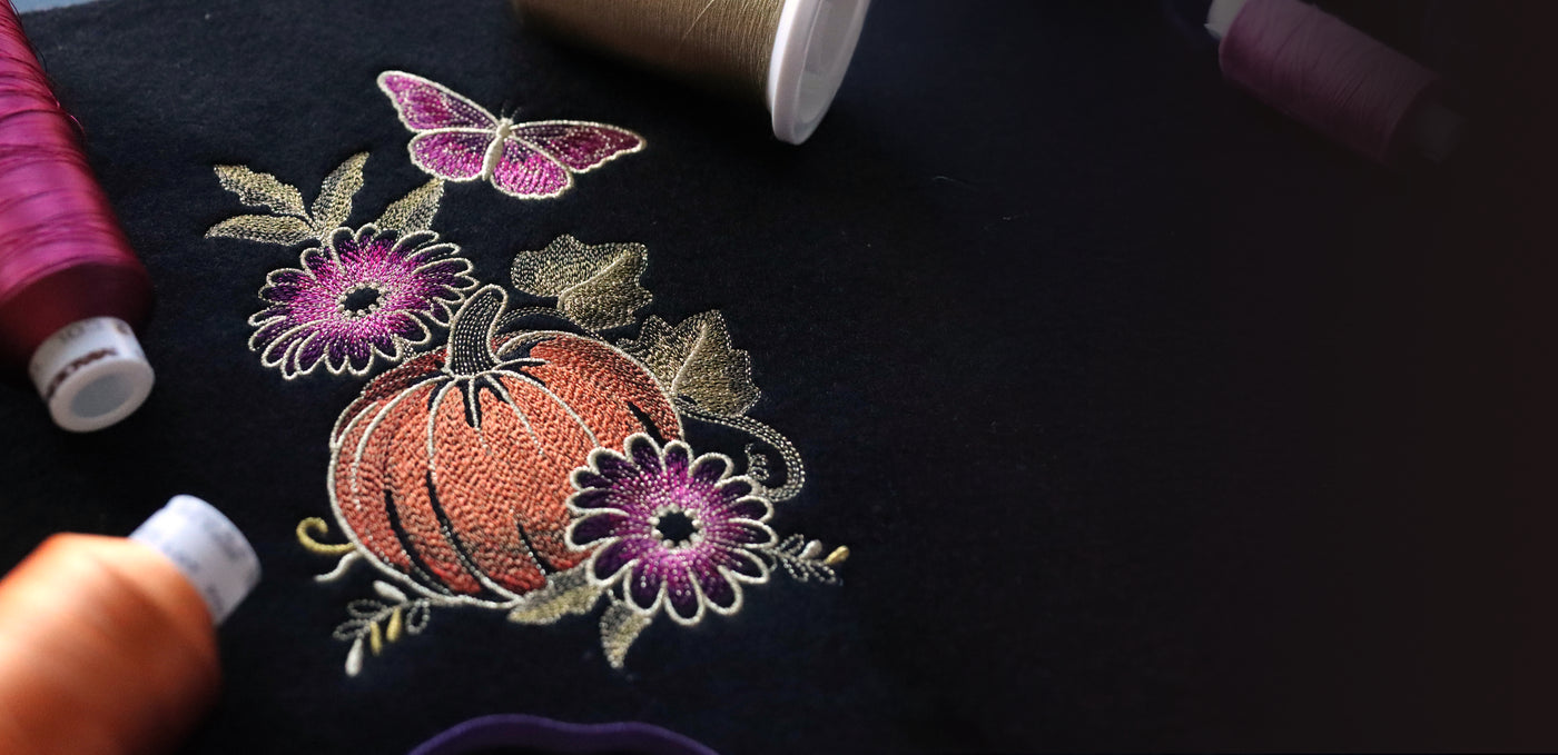 Machine embroidery design of a pumpkin, flowers, and butterfly on black fabric.