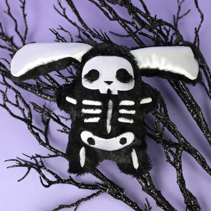 Machine embroidered skeleton plushie bunny on a purple background with black branches