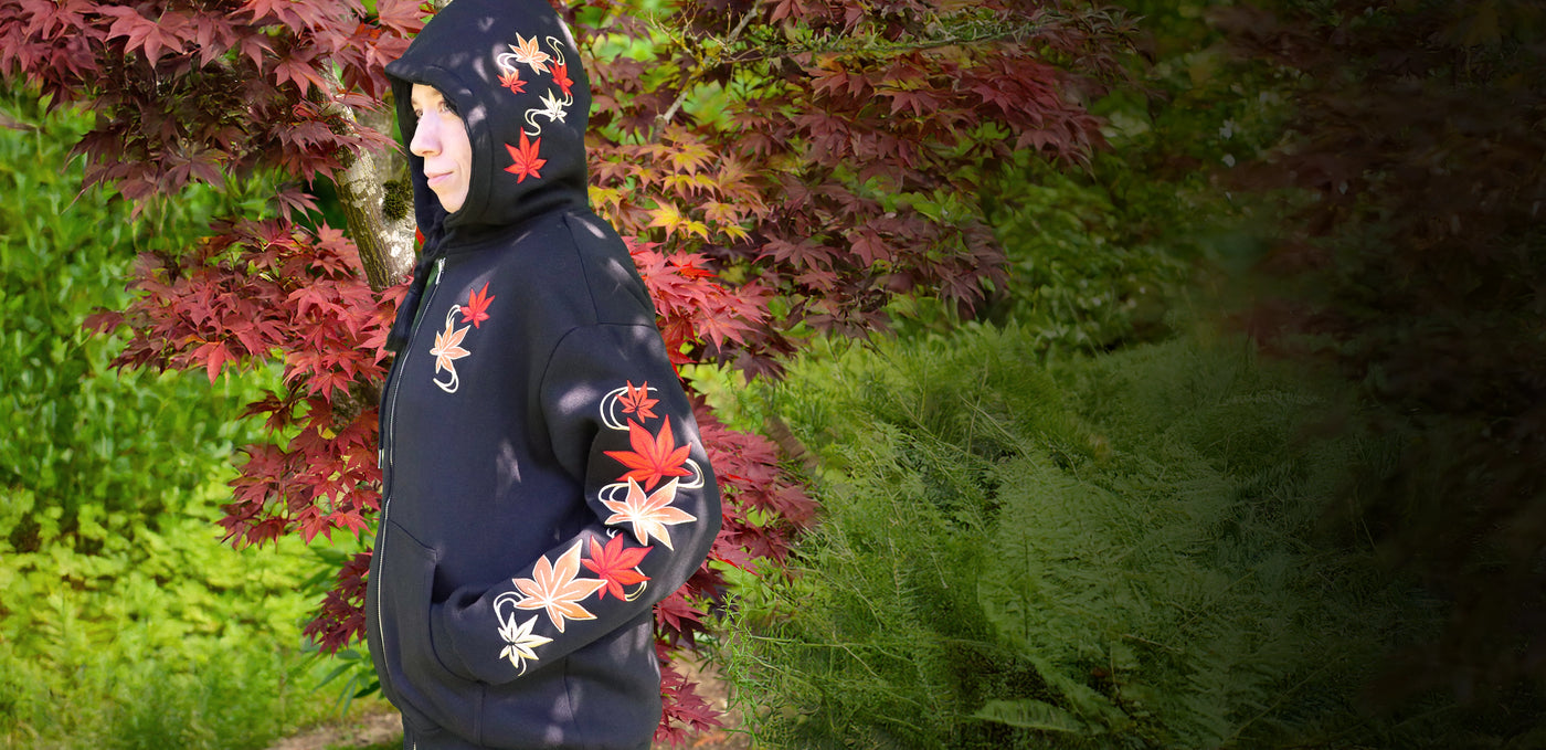 Person wearing a dark hoodie with colorful fall machine embroidery leaves in an outdoor setting