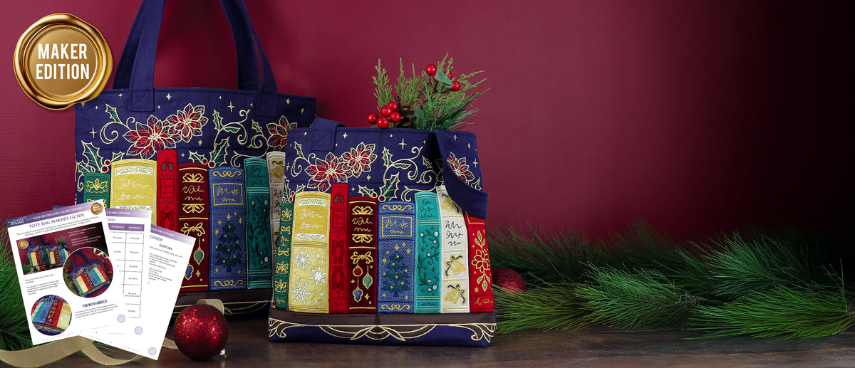 Two navy blue tote bags with embroidered colorful books, poinsettias, holly, and gold accents are displayed with evergreen branches and red ornaments.