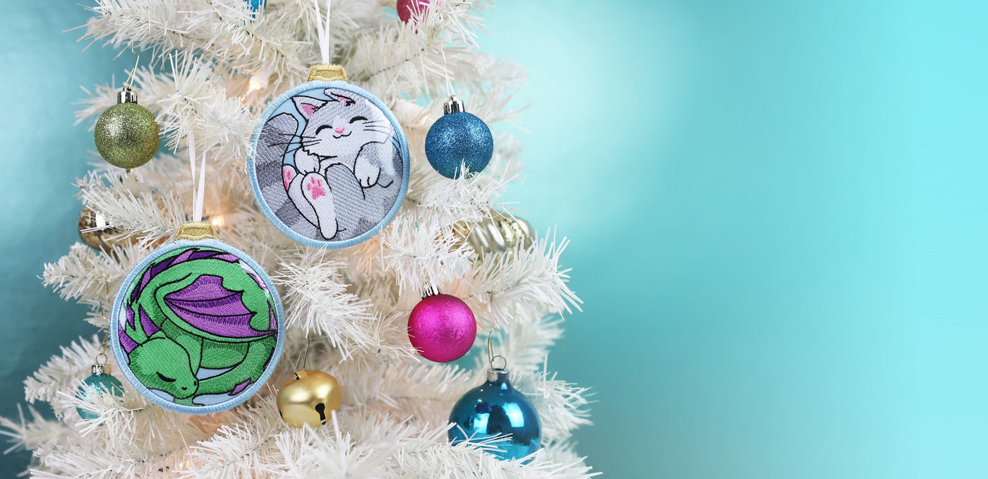 Machine embroidered dragon and cat in-the-hoop ornament on a white Christmas tree surrounded by ornaments.