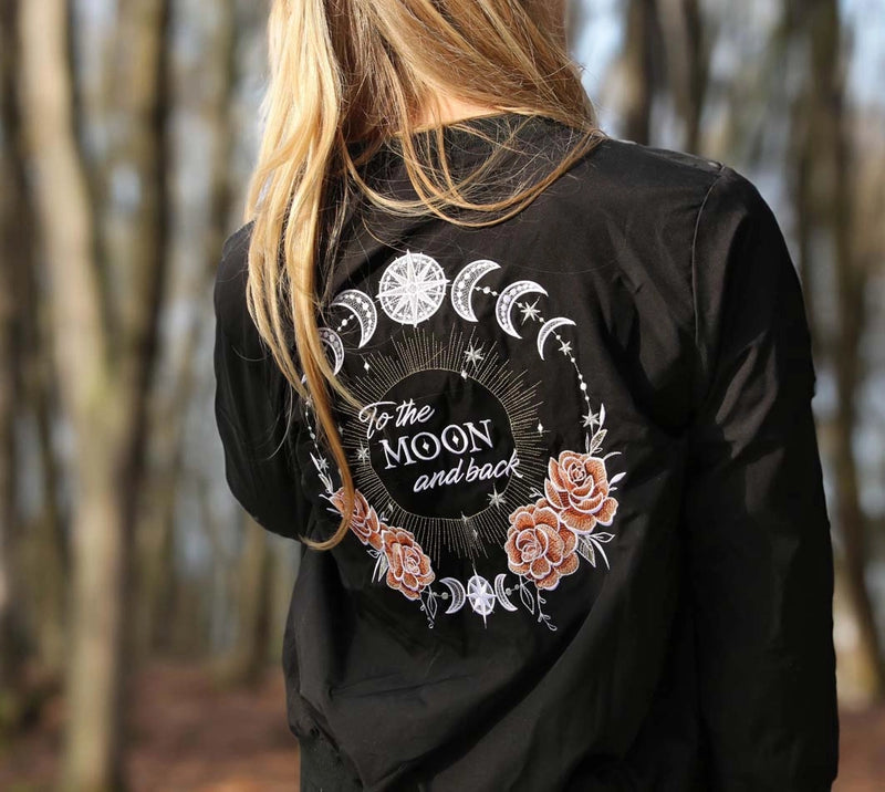 Person wearing a black jacket with celestial design and 'To the Moon and back' text in a forest setting
