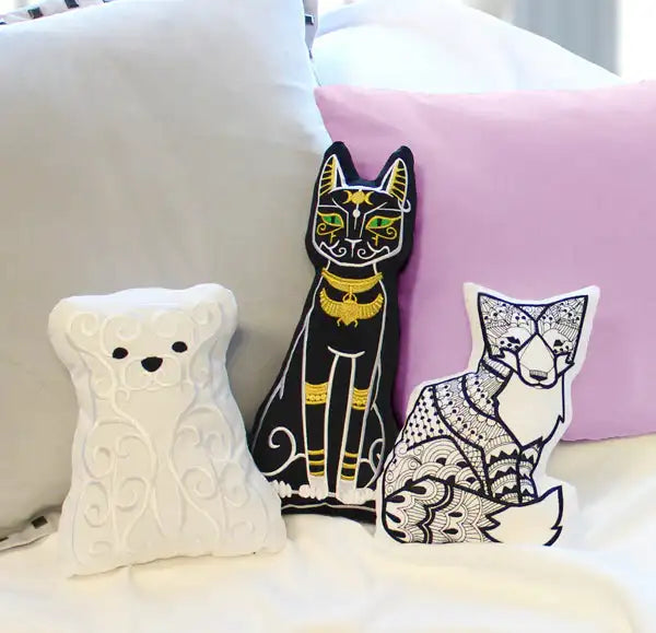 Three machine embroidery designs on pillows resting on a bed