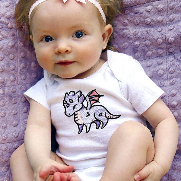 Baby wearing a white onesie with a machine embroidered dragon design on a purple textured blanket.