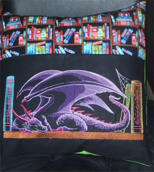 Machine embroidered dragon design on a black pillow with colorful bookshelf fabric.