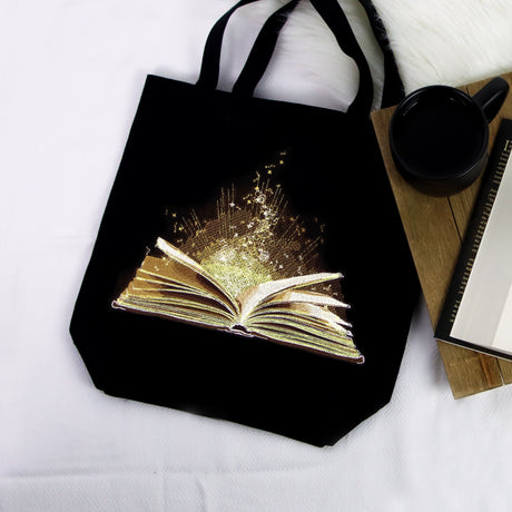 Black tote bag with a machine embroidery glowing book design on a white surface